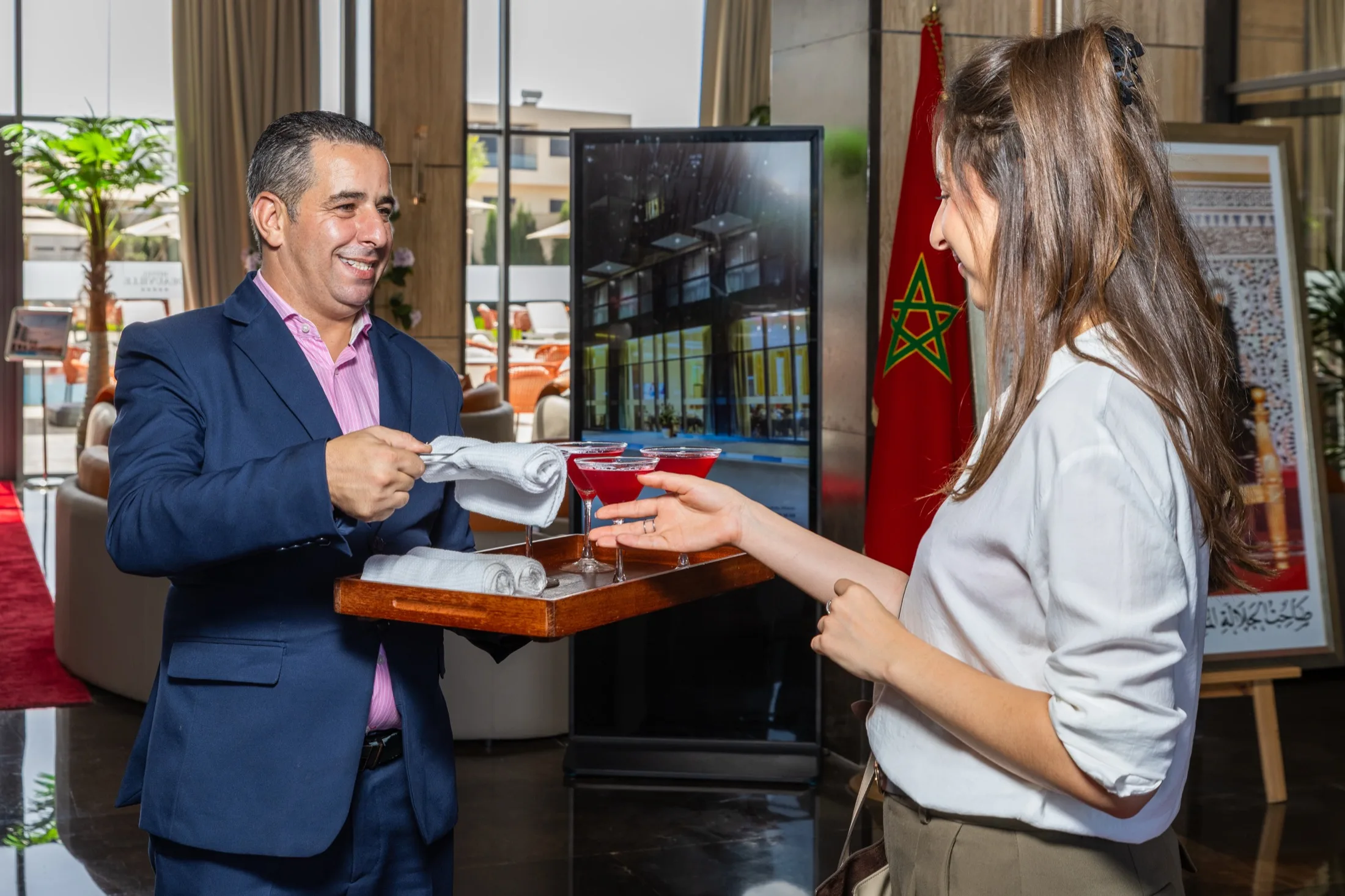 Un membre du personnel offre une boisson fraîche et une serviette rafraîchissante à une cliente, à son arrivée à l'hôtel